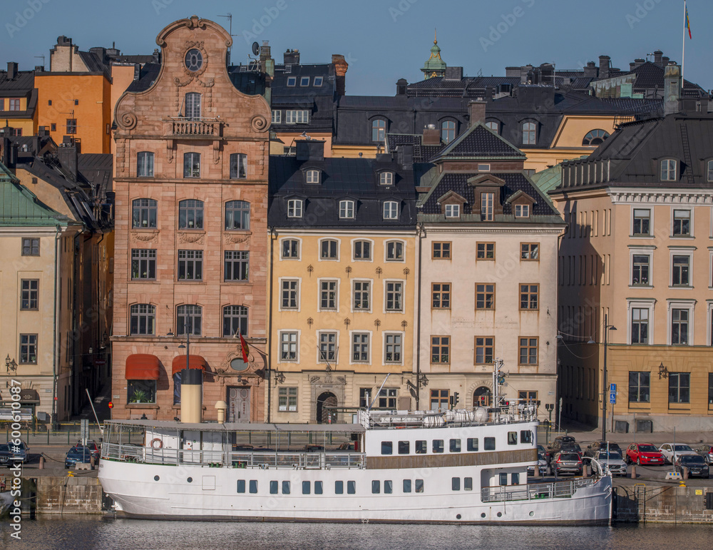 Old 1700s houses on the pier Skeppsbron in the old town Gamla Stan, an archipelago commuting ferry, a sunny early tranquil summer day in Stockholm