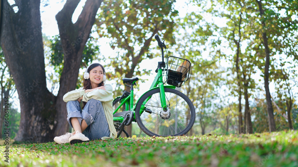 Women in headphone sitting on the grass to listening the music and resting after cycling in park Women in headphone sitting on the grass to listening the music and resting after cycling in park