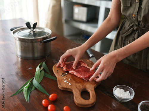 A woman in the kitchen prepares a dinner of meat and vegetables and spices on a wooden table against the backdrop of a stylish kitchen  close-up hands  fresh eco products  healthy nutrition  lifestyle