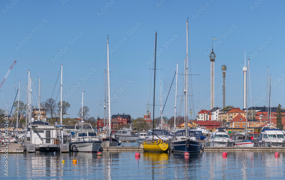 Boats in the bay Ryssviken, wharf island Beckholmen, boats and buildings and cranes, background church tower and towers of the Tivoli, a sunny early tranquil day in Stockholm