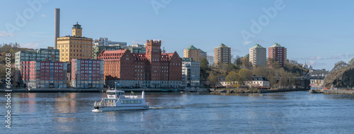 An archipelago commuter ferry passing the boat passage Danvikskanalen, skyscrapers on a hill, a sunny early tranquil summer day in Stockholm © Hans Baath