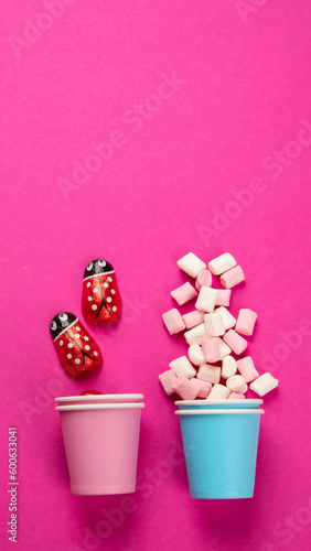 Paper cups with different candies on pink background.