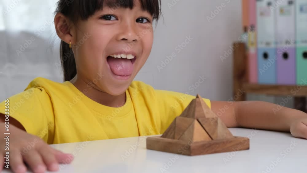 Asian cute little girl playing with wooden toy jigsaw puzzle pyramid on table. Healthy children training memory and thinking. Wooden puzzles are games that increase intelligence for children. Asian cute little girl playing with wooden toy jigsaw puzzle pyramid on table. Healthy children training memory and thinking. Wooden puzzles are games that increase intelligence for children.