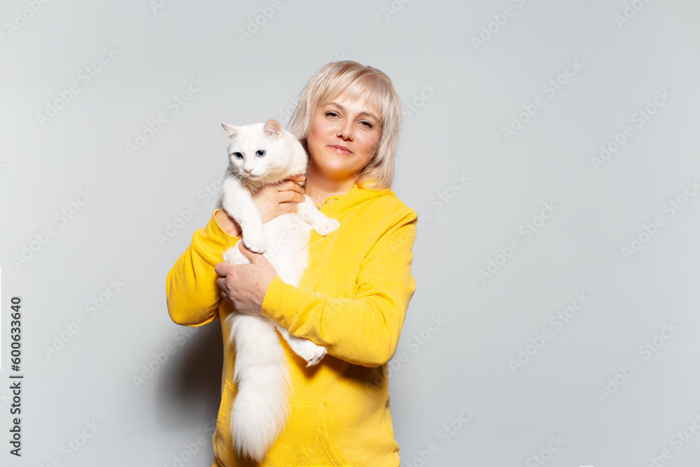 Studio portrait of happy blonde woman holding a fluffy cat with blue eyes on white background, wearing yellow sweater. Studio portrait of happy blonde woman holding a fluffy cat with blue eyes on white background, wearing yellow sweater.