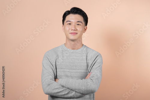 Young, handsome and friendly face man smile, dressed casually with happy and self-confident positive expression with crossed arms on beige background
