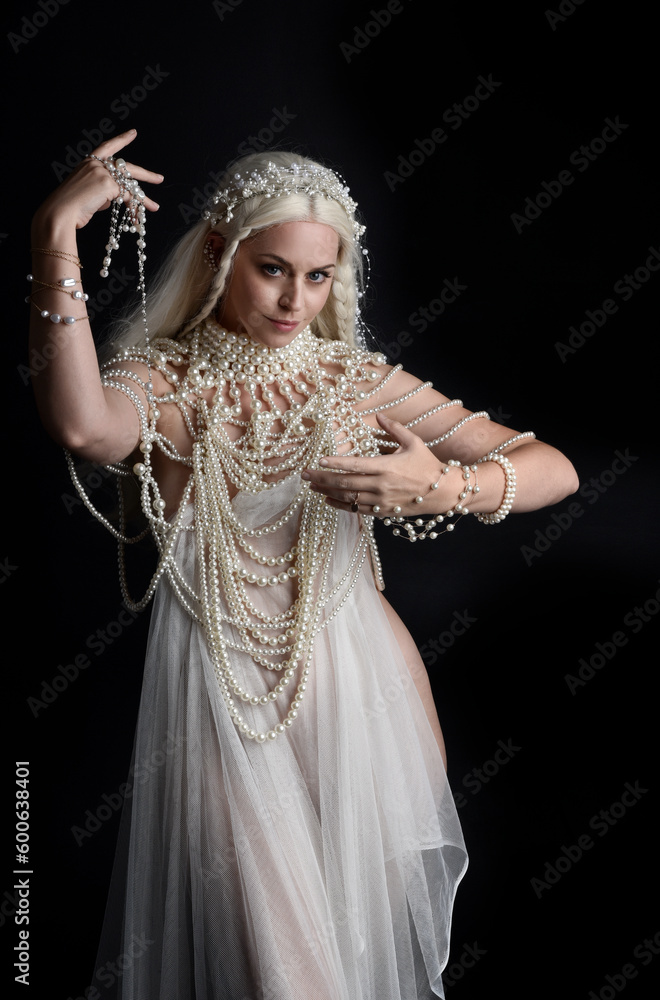 Close up portrait of beautiful blonde female model wearing an extravagant pearl jewelled gown. Gestural arms reaching out, isolated on a black studio background. Close up portrait of beautiful blonde female model wearing an extravagant pearl jewelled gown. Gestural arms reaching out, isolated on a black studio background.