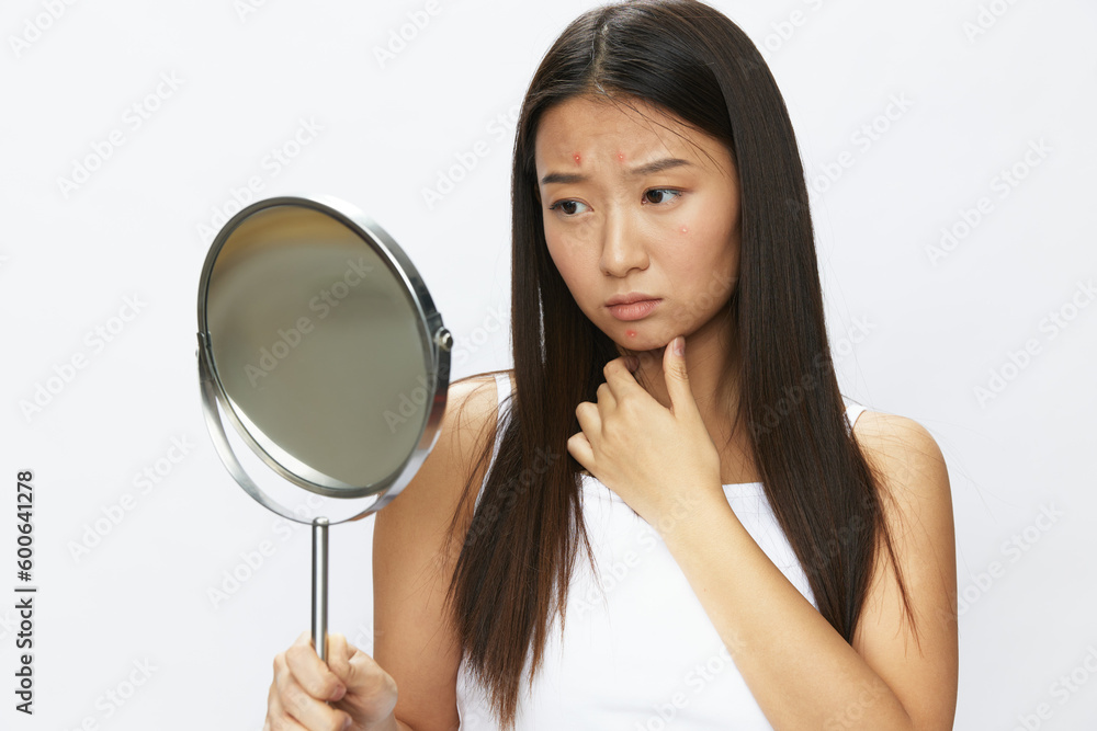 Asian woman with mirror in hand facial skin problems, acne and inflammation, red rash and allergies, chicken pox, sadness from rashes. Facial skin care concept for diseases and nerves Asian woman with mirror in hand facial skin problems, acne and inflammation, red rash and allergies, chicken pox, sadness from rashes. Facial skin care concept for diseases and nerves