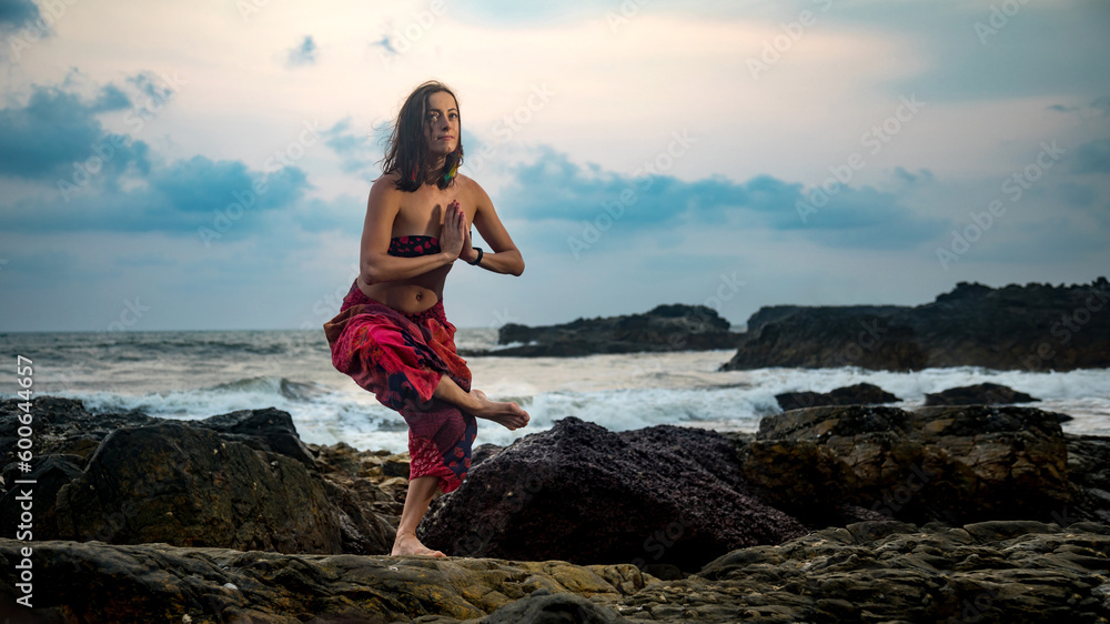 Young beautiful healthy woman making meditation on the rocks, sunset on the sea. Arambol, Goa, India.