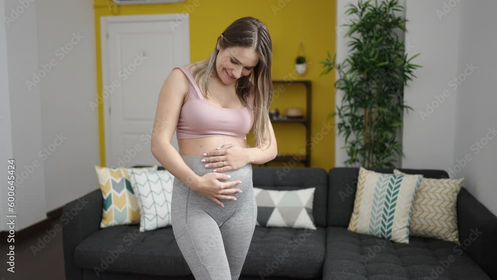 Young pregnant woman wearing sportswear touching belly at home Young pregnant woman wearing sportswear touching belly at home