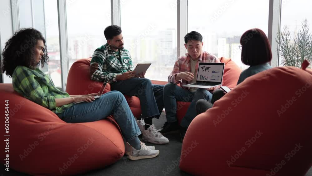 Team of confident entrepreneurs looking at laptop screen while gathering in coworking space with soft seats and devices. Data analysts brainstorming about budget allocations using infographics. Team of confident entrepreneurs looking at laptop screen while gathering in coworking space with soft seats and devices. Data analysts brainstorming about budget allocations using infographics.