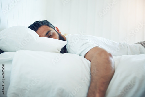 Tired, relax and a man on a bed for sleep, depression and fatigue at home. Rest, napping and a guy sleeping in the bedroom with insomnia, narcolepsy or depressed while lying looking exhausted photo