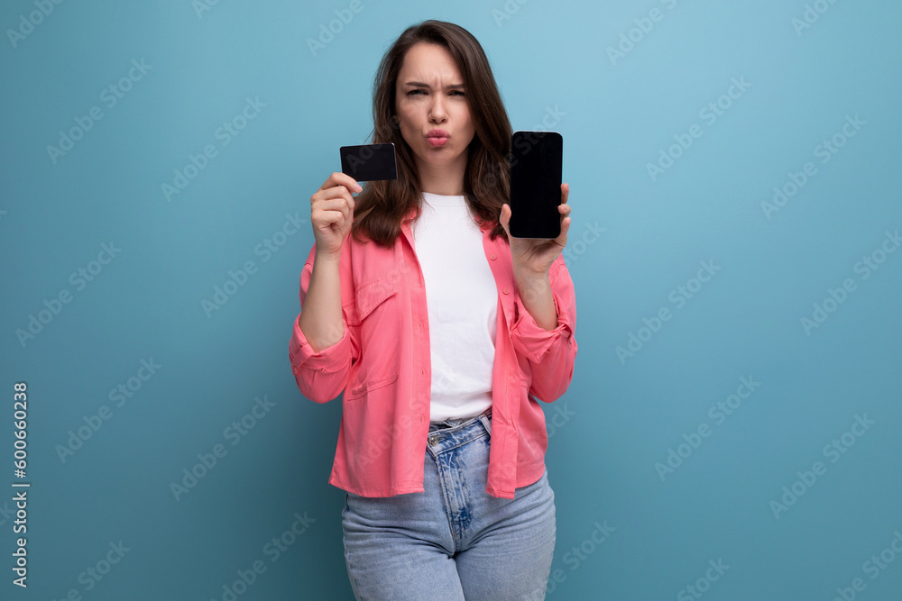 e-commerce business. brunette young woman in pink shirt and jeans with phone and money card mockup on studio isolated background e-commerce business. brunette young woman in pink shirt and jeans with phone and money card mockup on studio isolated background