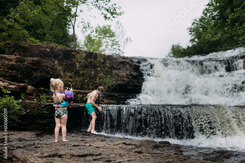 Child taking photos of brother playing in waterfall