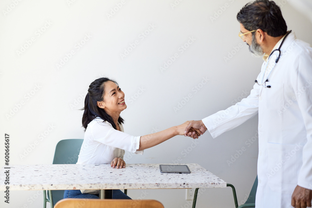 Mature male doctor doing handshake with female patient in clinic Mature male doctor doing handshake with female patient in clinic