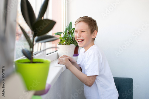 A cute boy stands near the window of a white balcony and laughs.