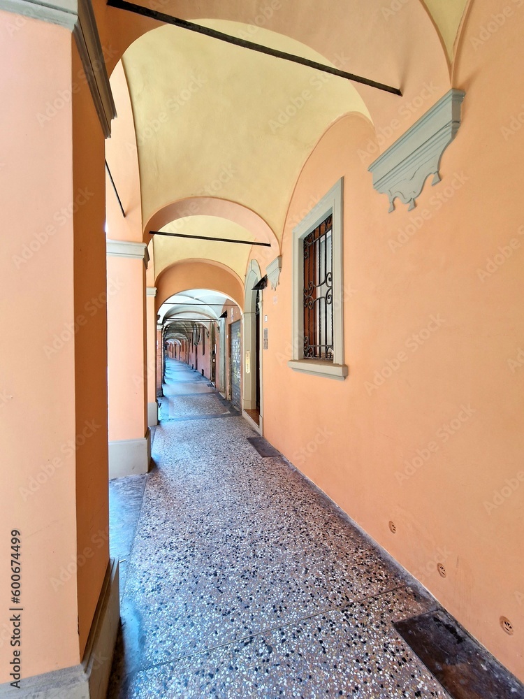 Fototapeta premium Portico in bright yellow or orange (light) colors in Bologna, Italy, with marble floor and arched stone walls - metal bars in front of window for safety
