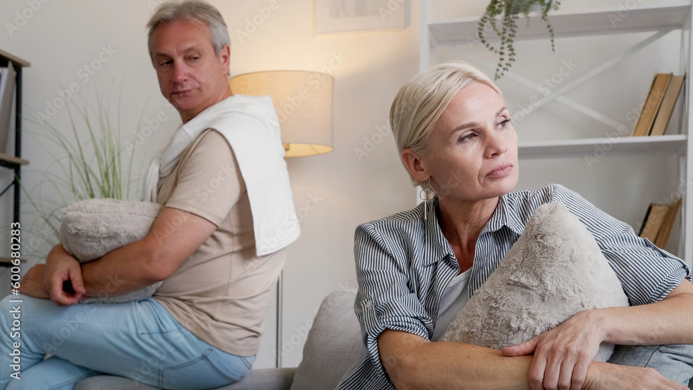Obraz premium Family quarrel. Offended couple. Disagreement problem. Angry middle-aged man and woman sitting sofa turning back each other in light home interior.