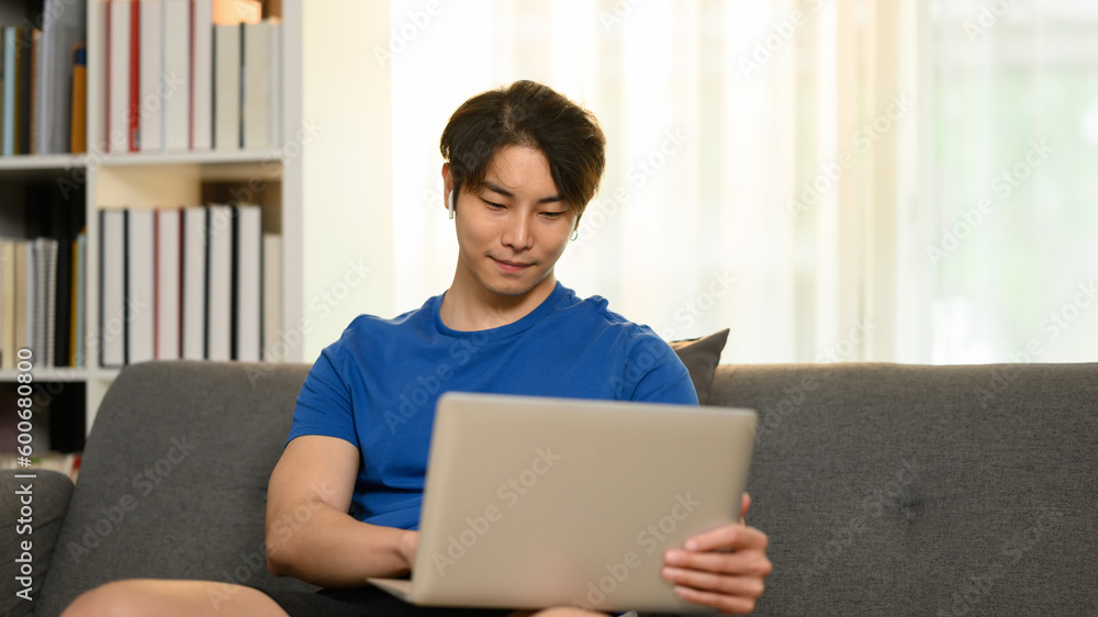 Asian man freelancer sitting on couch and using laptop. Communication, people, technology concept Asian man freelancer sitting on couch and using laptop. Communication, people, technology concept