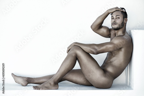 Portrait, nude and a sexy man sitting on the floor of a studio against a white background for natural body care. Fitness, skin and wellness with a handsome young male model posing naked for health