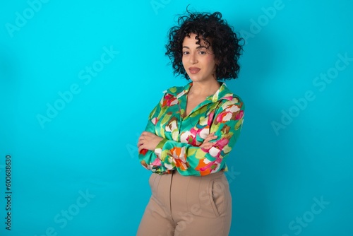 young arab woman wearing colorful shirt over blue background happy face smiling with crossed arms looking at the camera. Positive person.