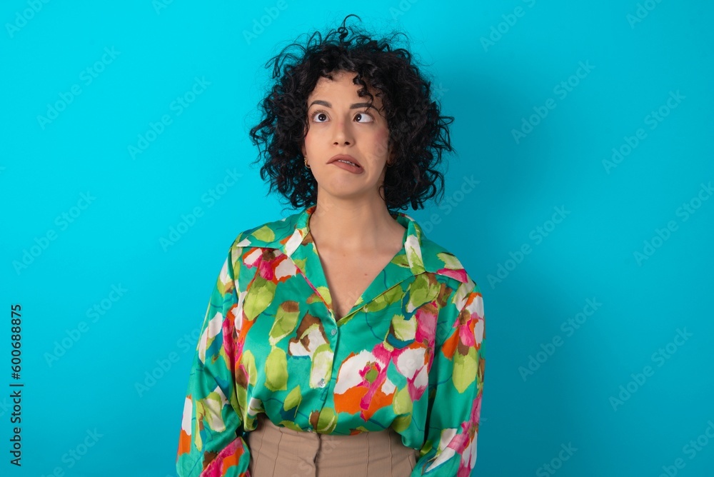 young arab woman wearing colorful shirt over blue background making grimace and crazy face, screaming out of control, funny lunatic expressing freedom and wild. young arab woman wearing colorful shirt over blue background making grimace and crazy face, screaming out of control, funny lunatic expressing freedom and wild.