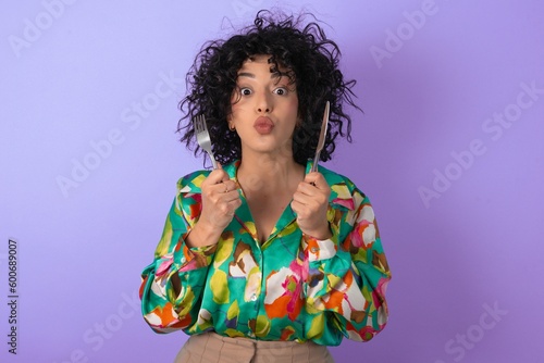 hungry young arab woman wearing colorful shirt over blue background holding in hand fork knife want tasty yummy pizza pie