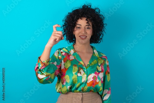 young arab woman wearing colorful shirt over blue background pointing up with fingers number nine in Chinese sign language Jiu photo
