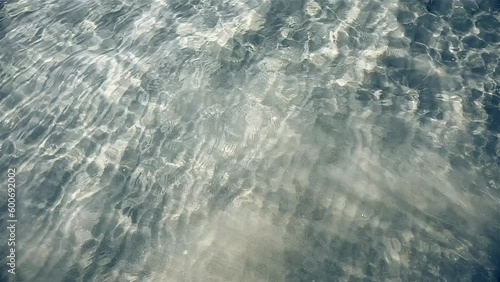 Sea surface closeup slow motion. Rays of sun shining on the sea. Small ripples on the water, Sandy sea bottom Caustic effect, Seamless loop.