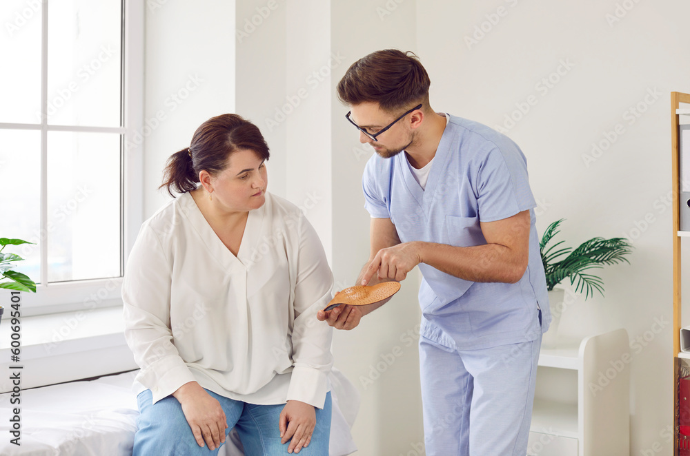 Obraz premium Man doctor podiatrist at the clinic gives comfortable orthotic medical insoles for orthopedic shoes to a young overweight woman patient. Feet health, flat foot prevention concept