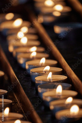 Close-up shot of multiple lit votive candles in a church setting, with a blurred out background photo