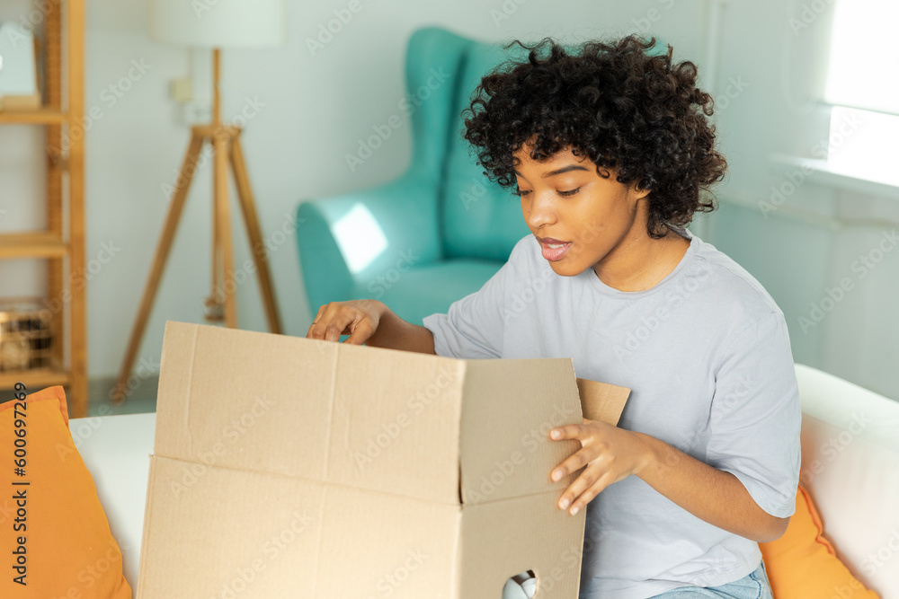 African girl unpacking delivery looking in box. Happy woman opening carton box. Female getting parcel looking at delivered goods items. Satisfied client positive feedback quick express deliver African girl unpacking delivery looking in box. Happy woman opening carton box. Female getting parcel looking at delivered goods items. Satisfied client positive feedback quick express deliver