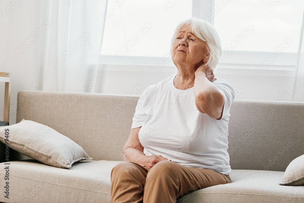Elderly woman severe neck pain sitting on the sofa, health problems in old age, poor quality of life. Elderly woman severe neck pain sitting on the sofa, health problems in old age, poor quality of life.