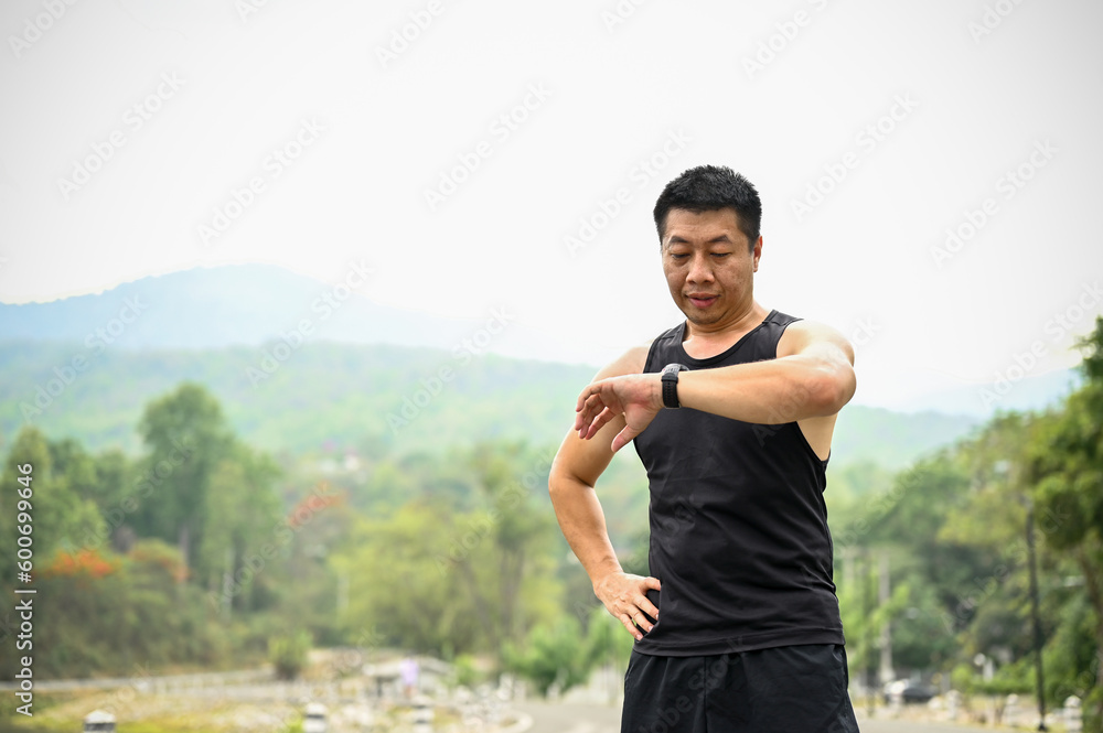 A mature Asian man checking his running miles on his smartwatch while jogging A mature Asian man checking his running miles on his smartwatch while jogging