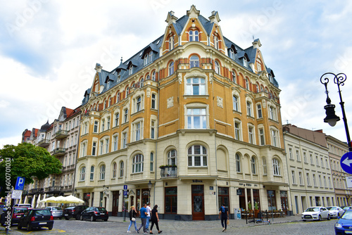 Old architectural corner building with beige and orange walls  windows and a blue roof. City street with cars and people. Summer cloudy day.  Poland  Poznan  June 2022