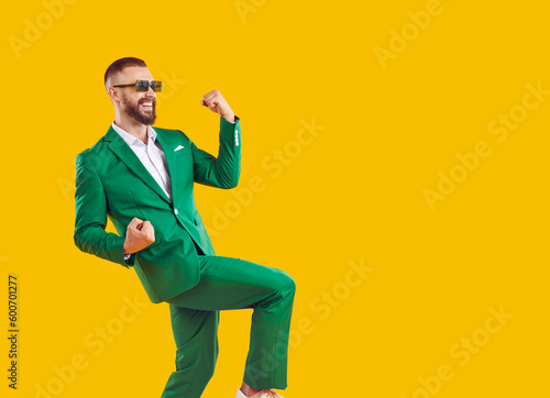 Yes, awesome, cool. Side view of happy smiling overjoyed handsome man wearing trendy green suit and spectacles dancing isolated on yellow copy space background, celebrating success and having fun