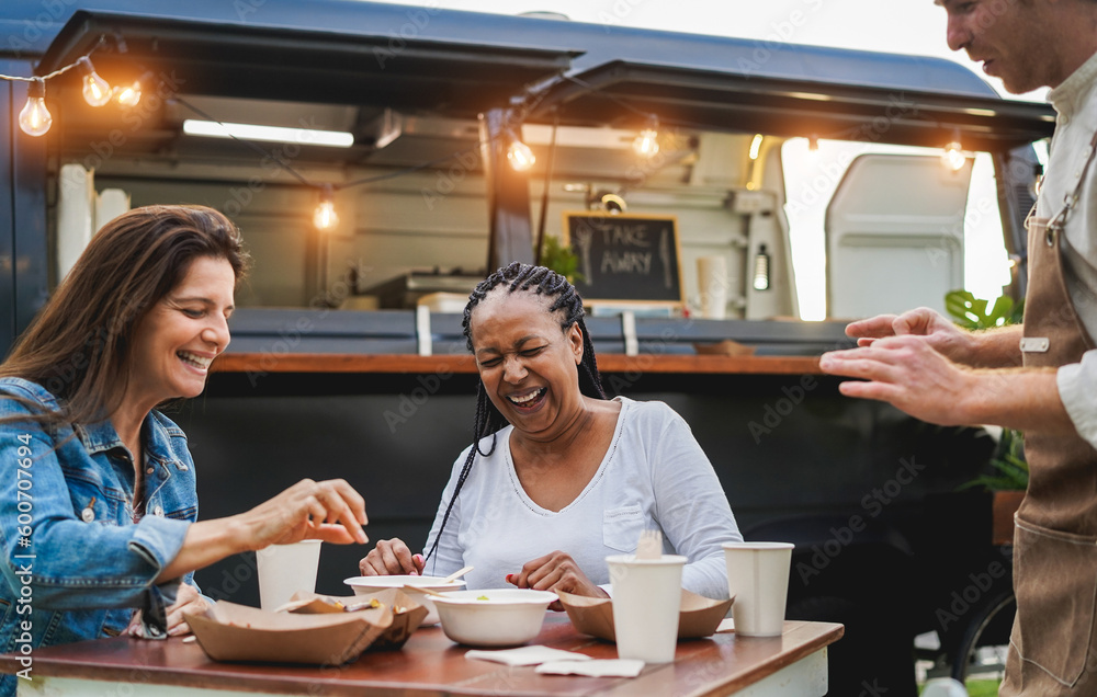 Multiracial women eating at food truck restaurant outdoor - Focus on african senior female face Multiracial women eating at food truck restaurant outdoor - Focus on african senior female face