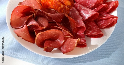meat slices on a plate. traditional spanish sausage with beef jerky closeup. salchichon, chorizo and prosciutto on a light background. serving cold cuts. antipasto in sunlight.