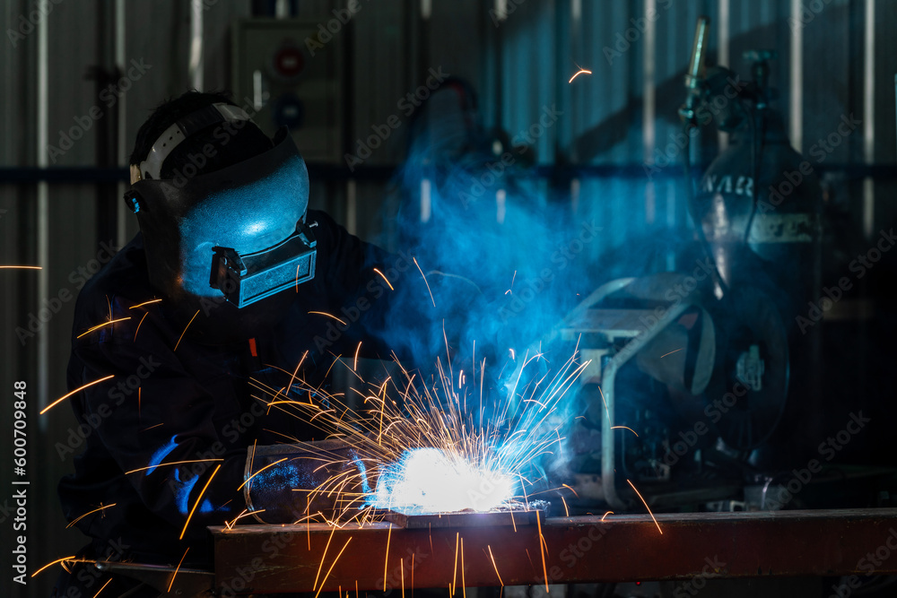 A craftsman or workers wearing industrial uniforms and welded iron mask at steel welding plants, Industrial safety first concept. A craftsman or workers wearing industrial uniforms and welded iron mask at steel welding plants, Industrial safety first concept.
