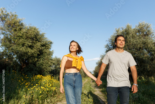 Outdoor shot of young couple in love walking on pathway through grass field. Man and woman walking along grass field.
