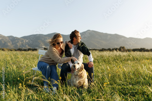 Wallpaper Mural Young happy couple with dog, sitting on chairs in feather grass field on summer sunset day Torontodigital.ca
