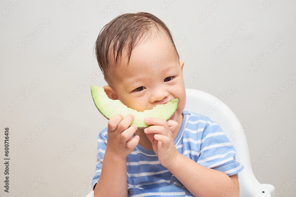 Portrait of Cute Smiling Asian 18 months, 1 year old toddler baby boy child eating melon, Little kid sitting in high chair eating fruit, Healthy snack and Self feeding concept Portrait of Cute Smiling Asian 18 months, 1 year old toddler baby boy child eating melon, Little kid sitting in high chair eating fruit, Healthy snack and Self feeding concept
