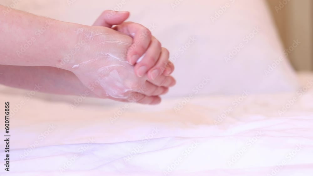 Girl applies the cream on the skin against the background of bed linen. Anti aging skin care cosmetics. Hands close-up, the girl applies a moisturizer and massages her hand for softness Girl applies the cream on the skin against the background of bed linen. Anti aging skin care cosmetics. Hands close-up, the girl applies a moisturizer and massages her hand for softness