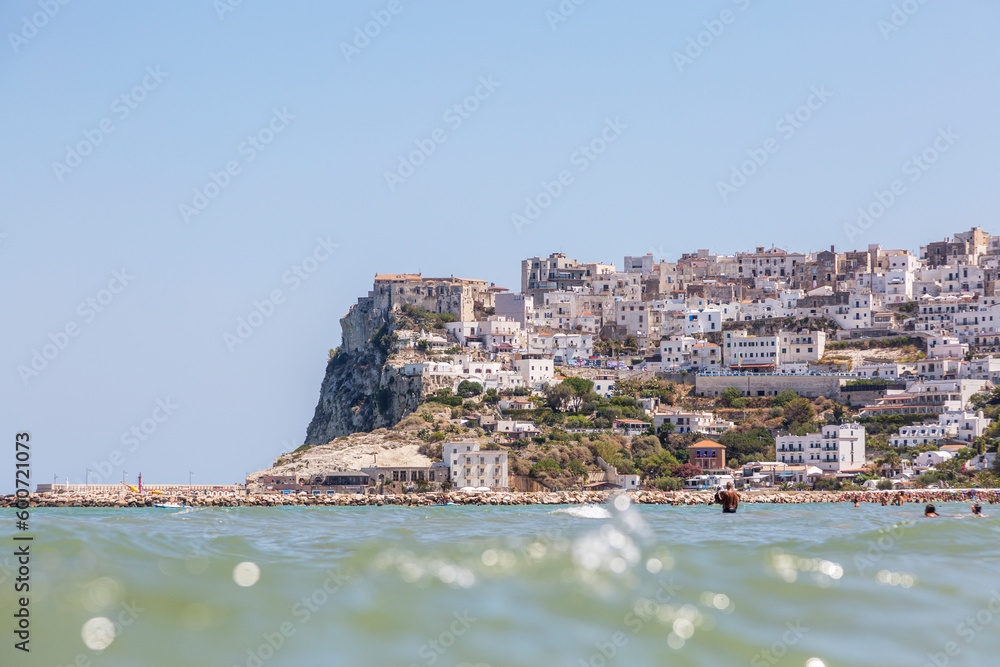 A sea beach with people who rest in the summer on it and buildings of Peschici, Puglia A sea beach with people who rest in the summer on it and buildings of Peschici, Puglia