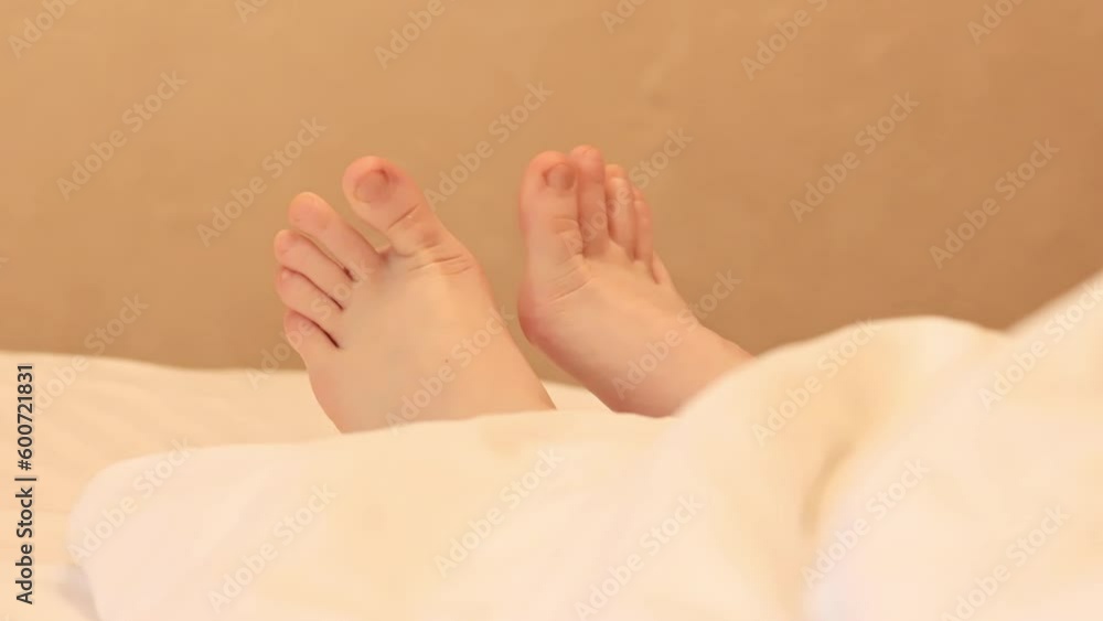 Morning in the bedroom, women's legs under a white blanket. Healthy sleep relaxation, lazy morning concept. Resting in hotel concept. The toes of a woman in bed peek out from behind white linen Morning in the bedroom, women's legs under a white blanket. Healthy sleep relaxation, lazy morning concept. Resting in hotel concept. The toes of a woman in bed peek out from behind white linen