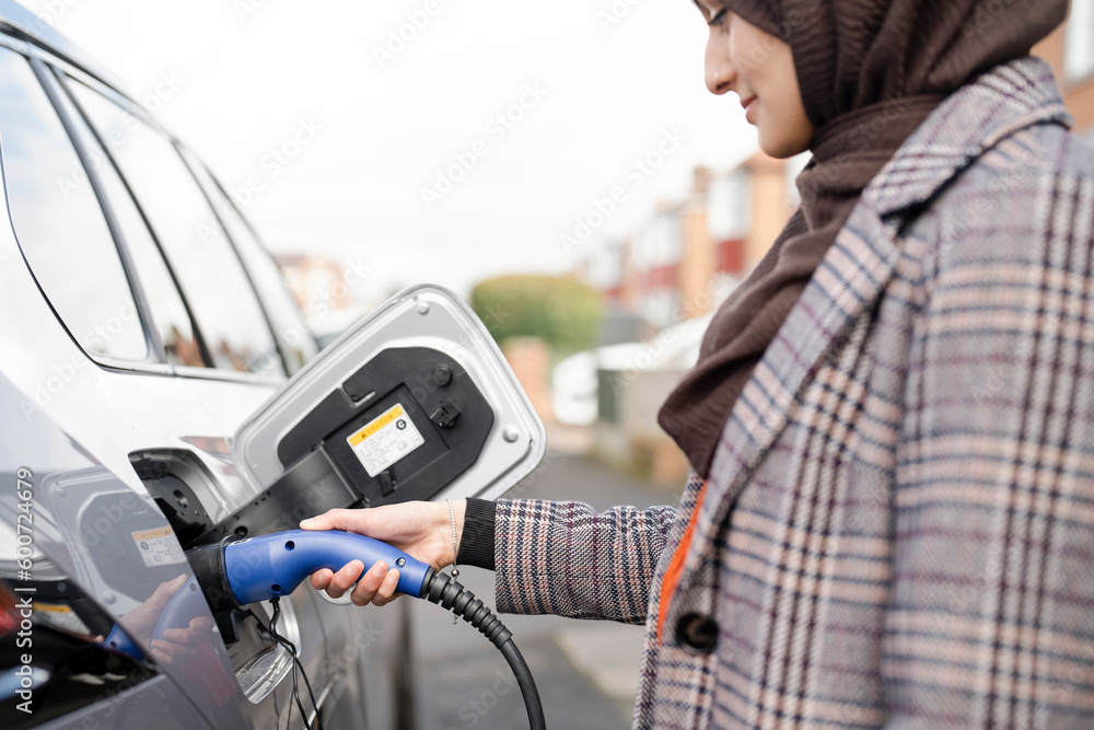 Woman wearing hijab charging electric car Woman wearing hijab charging electric car