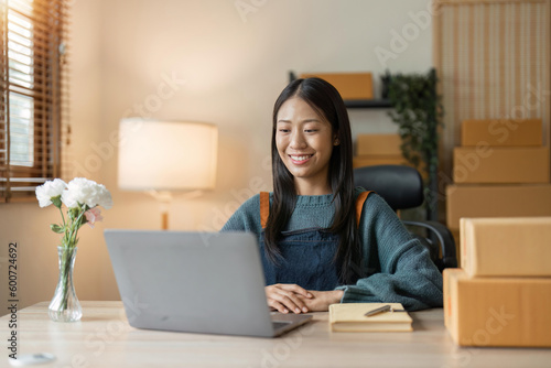 Young asian woman startup small business freelance sitting with parcel box and computer laptop in living room at home, Online marketing packing box delivery concept