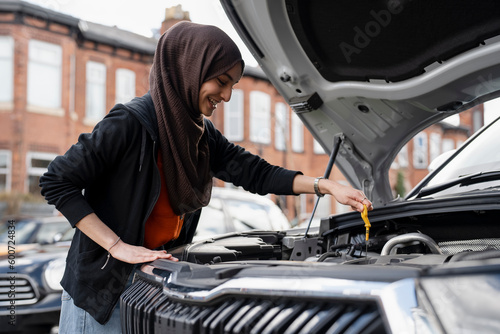 Woman wearing hijab checking oil in car engine