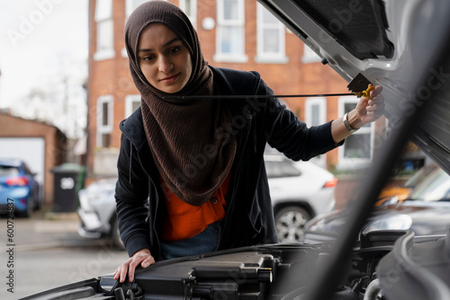 Woman wearing hijab looking into car engine