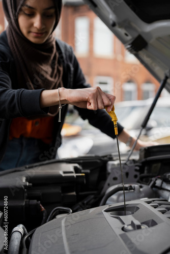 Woman wearing hijab checking oil in car engine