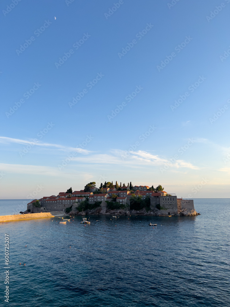 Boats float in the sea near the island of Sveti Stefan against a clear horizon. Montenegro